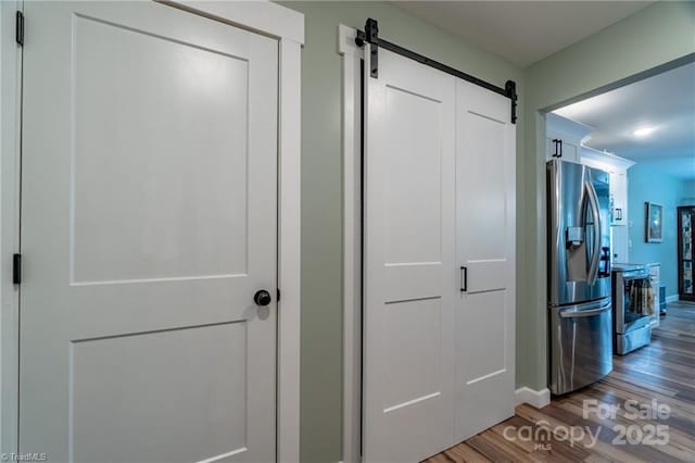 hall featuring wood finished floors, baseboards, and a barn door