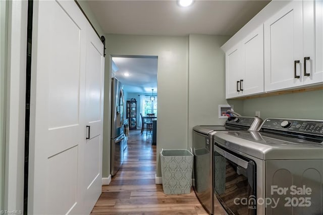 laundry area featuring cabinet space, a barn door, light wood-style flooring, and washer and dryer