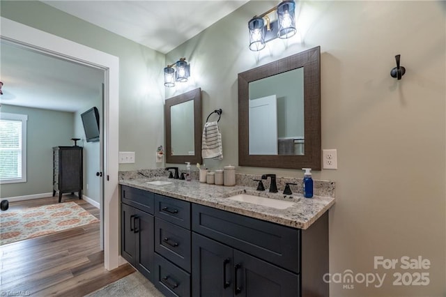 full bathroom with double vanity, baseboards, a sink, and wood finished floors