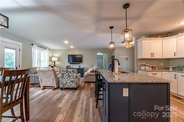 kitchen featuring light wood-style floors, open floor plan, white cabinets, a sink, and light stone countertops