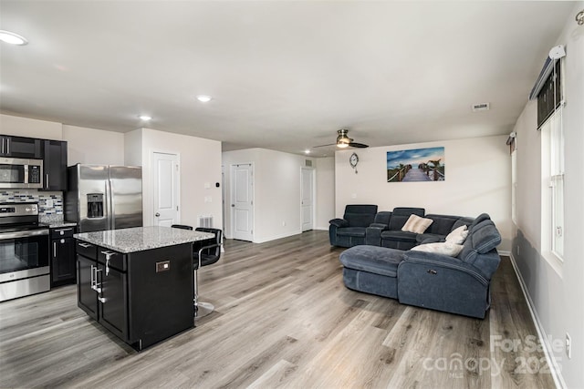 kitchen with light wood finished floors, stainless steel appliances, dark cabinetry, and a center island