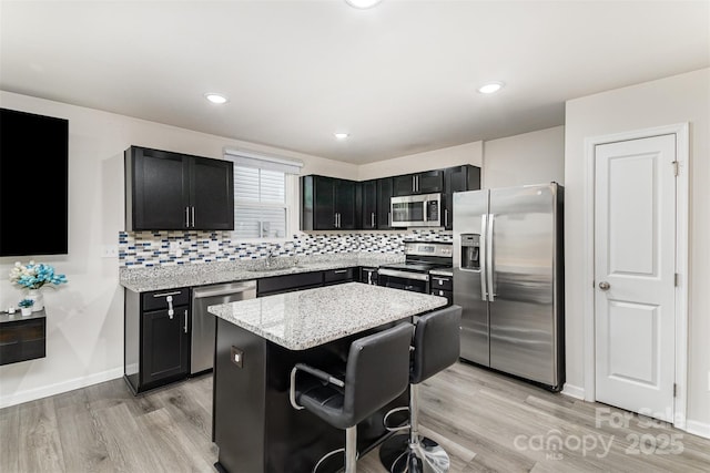 kitchen featuring light stone countertops, dark cabinets, stainless steel appliances, decorative backsplash, and a center island