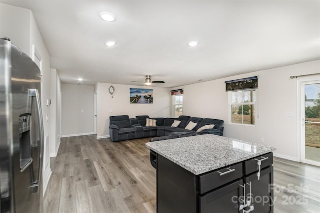 kitchen with baseboards, stainless steel fridge with ice dispenser, light stone counters, dark cabinetry, and light wood-type flooring