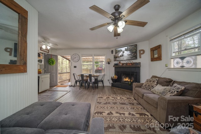 living room featuring ceiling fan, a fireplace, and wood finished floors