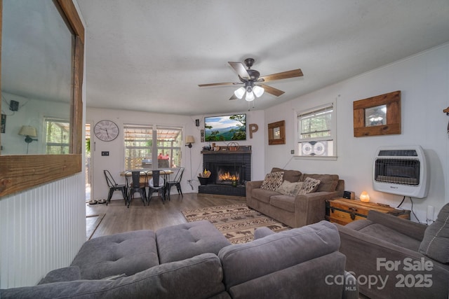 living area with heating unit, a brick fireplace, a wealth of natural light, and wood finished floors