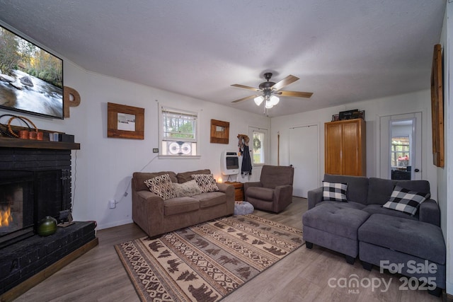 living room with heating unit, a ceiling fan, a brick fireplace, wood finished floors, and baseboards