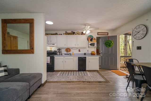 kitchen featuring under cabinet range hood, light countertops, light wood-type flooring, black appliances, and white cabinetry