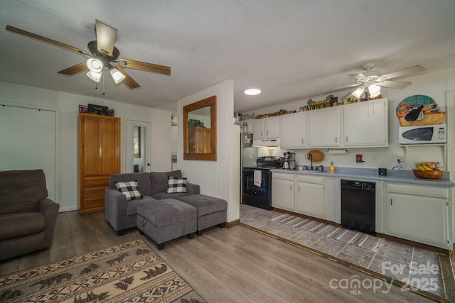 kitchen featuring black appliances, under cabinet range hood, open floor plan, and light wood-style floors