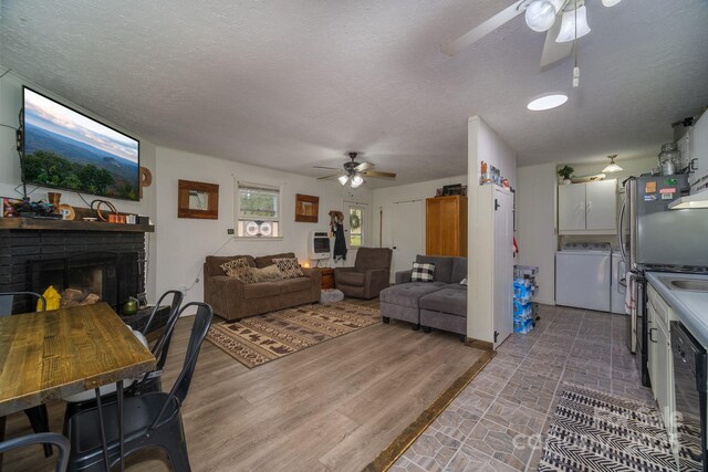 living room with a textured ceiling, ceiling fan, wood finished floors, independent washer and dryer, and a brick fireplace