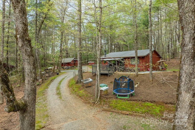 exterior space featuring an outbuilding, driveway, a trampoline, and a forest view