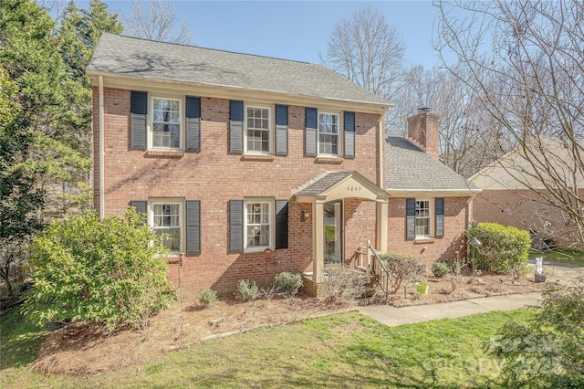 view of front of house with a front lawn, brick siding, a chimney, and a shingled roof