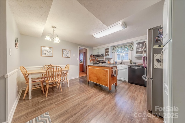 kitchen with a textured ceiling, glass insert cabinets, wood finished floors, freestanding refrigerator, and dishwashing machine