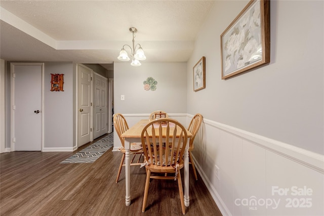 dining room featuring an inviting chandelier, wood finished floors, a wainscoted wall, and a textured ceiling