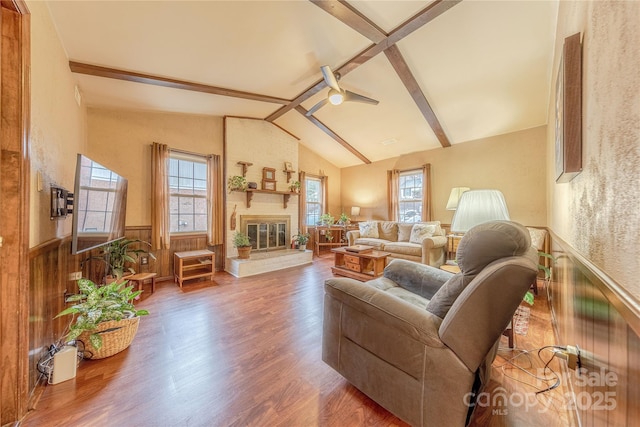 living area with a brick fireplace, vaulted ceiling with beams, a wainscoted wall, wood walls, and wood finished floors