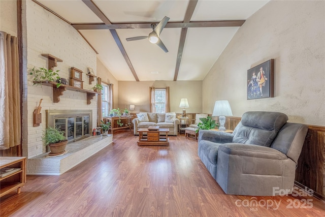 living room with a fireplace, lofted ceiling with beams, wood finished floors, and ceiling fan