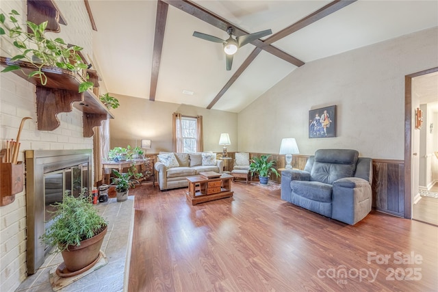 living room featuring a brick fireplace, vaulted ceiling with beams, a ceiling fan, and wood finished floors