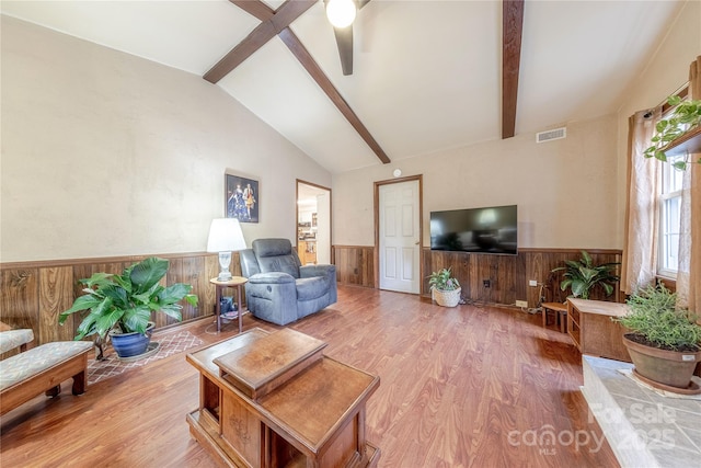 living room with wooden walls, wood finished floors, visible vents, a wainscoted wall, and lofted ceiling with beams