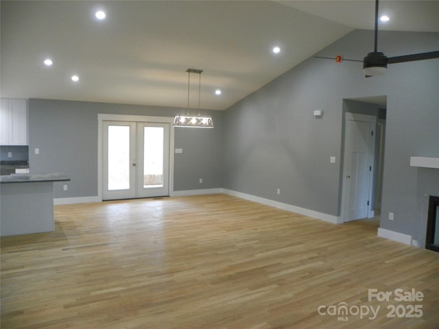 unfurnished living room featuring vaulted ceiling, french doors, light wood-style floors, a fireplace, and recessed lighting