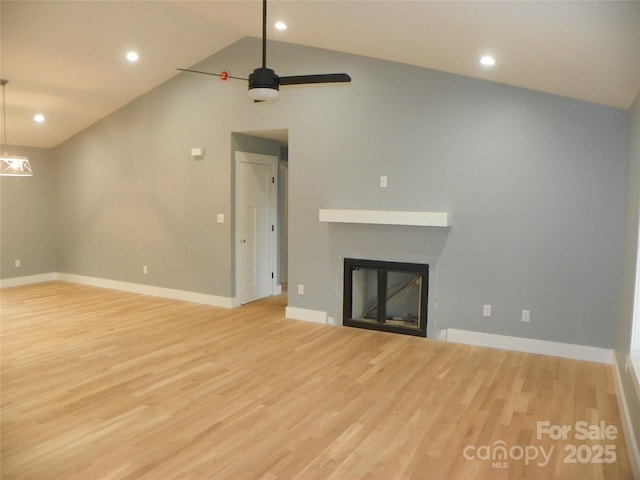 unfurnished living room with a glass covered fireplace, lofted ceiling, baseboards, and wood finished floors