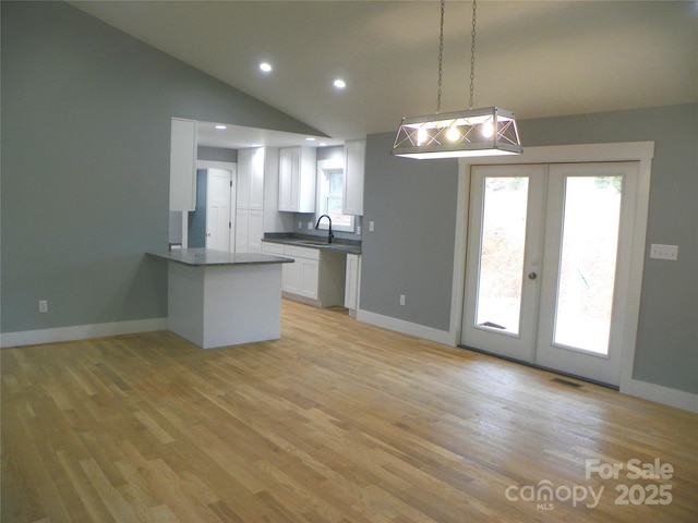 kitchen with white cabinets, a peninsula, vaulted ceiling, french doors, and a sink