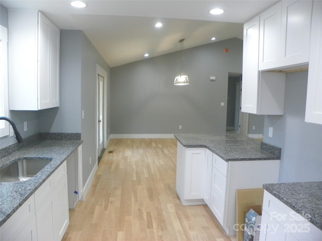 kitchen featuring vaulted ceiling, a sink, and white cabinetry