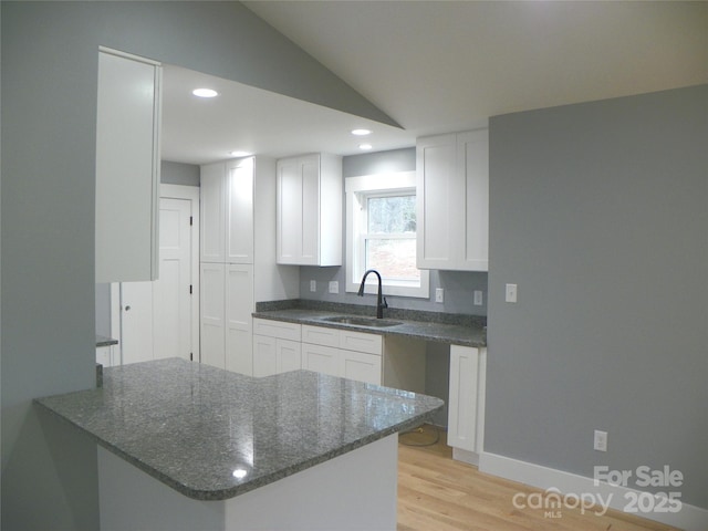 kitchen with white cabinets, vaulted ceiling, a sink, dark stone countertops, and a peninsula