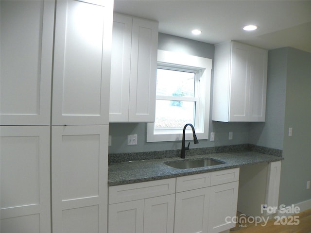 kitchen featuring dark stone countertops, white cabinets, a sink, and recessed lighting