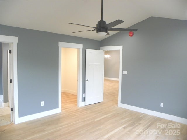 unfurnished bedroom with baseboards, lofted ceiling, ceiling fan, a spacious closet, and light wood-type flooring