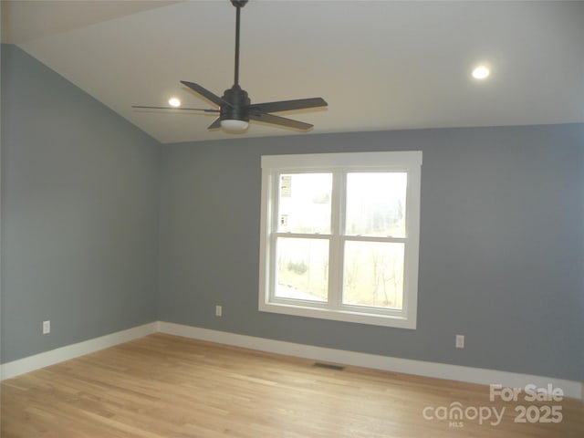 spare room featuring light wood finished floors, baseboards, visible vents, a ceiling fan, and vaulted ceiling