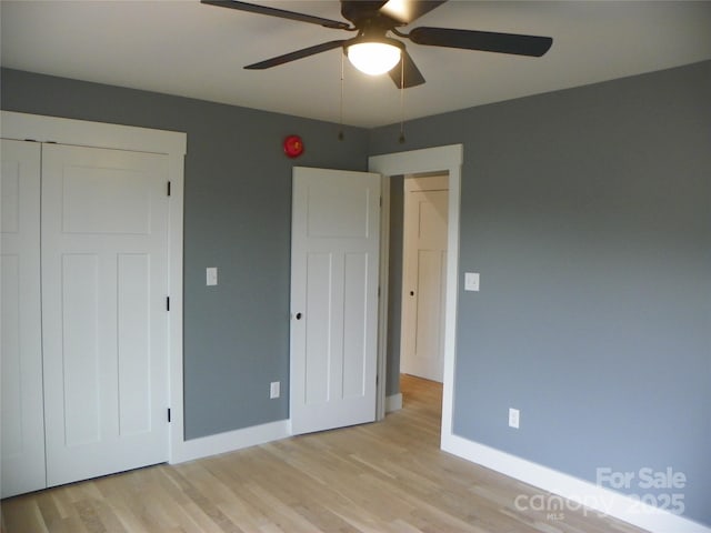 unfurnished bedroom featuring a ceiling fan, a closet, light wood-style flooring, and baseboards