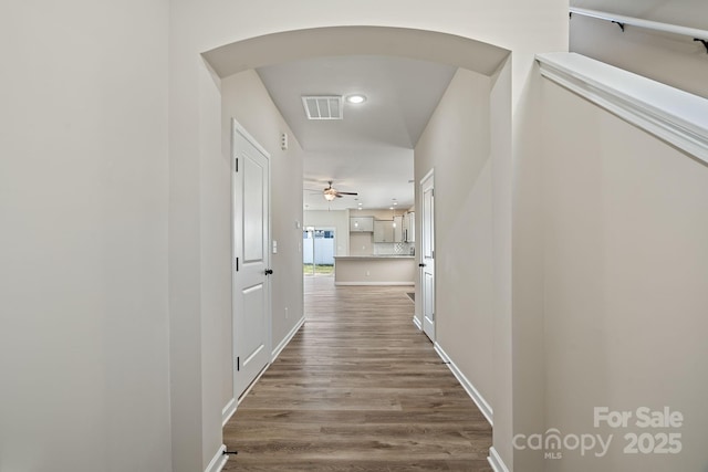 corridor featuring arched walkways, dark wood-type flooring, visible vents, and baseboards