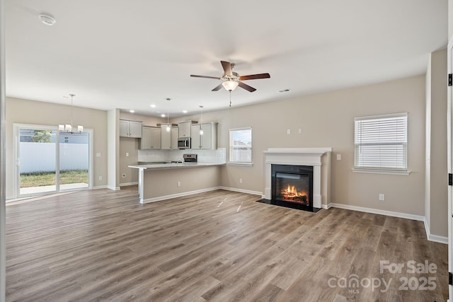 unfurnished living room with visible vents, light wood-style flooring, a fireplace with flush hearth, ceiling fan, and baseboards