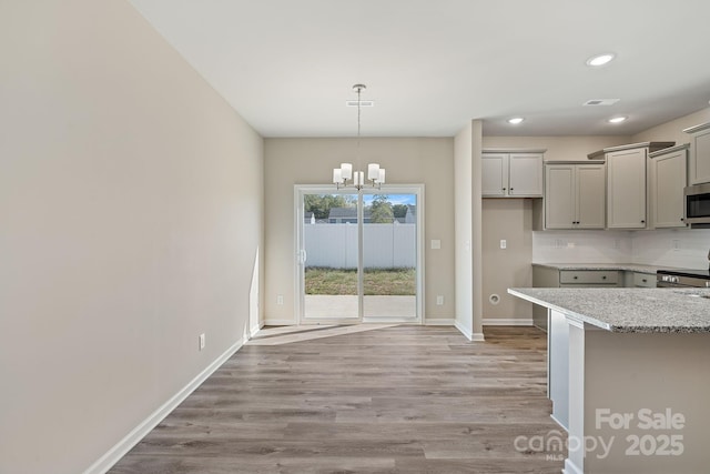 kitchen with baseboards, decorative backsplash, stainless steel microwave, gray cabinetry, and light wood-type flooring