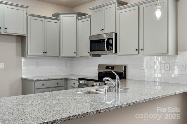 kitchen with stainless steel appliances, backsplash, gray cabinetry, a sink, and light stone countertops