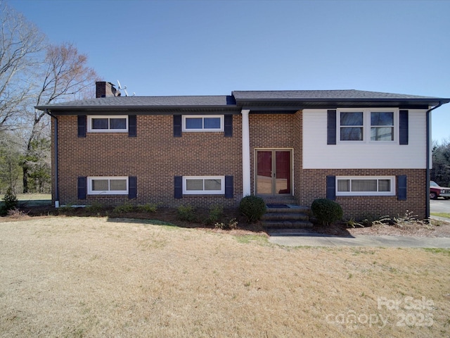 bi-level home featuring brick siding, a chimney, and a front yard