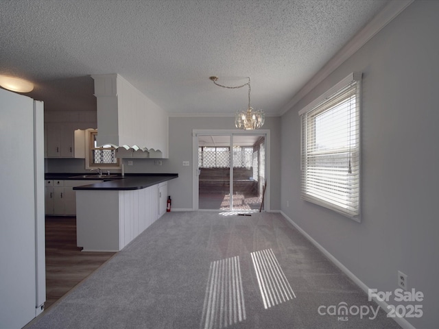 kitchen featuring baseboards, a peninsula, white cabinetry, dark countertops, and a notable chandelier