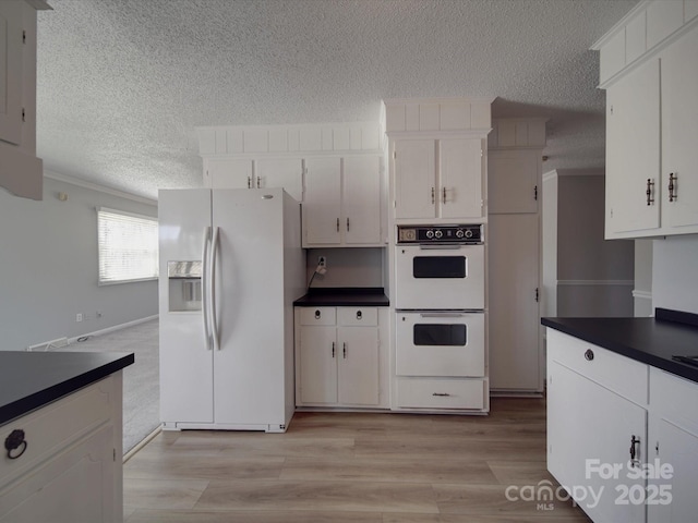 kitchen with a textured ceiling, white appliances, dark countertops, and white cabinetry