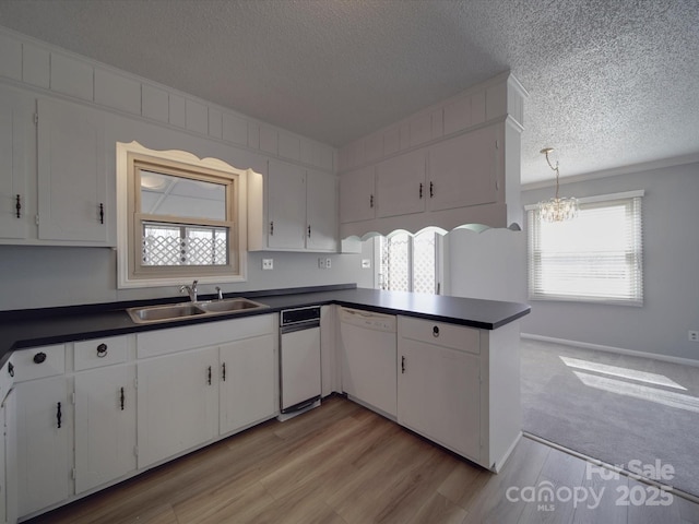 kitchen with dishwasher, dark countertops, white cabinetry, and a sink