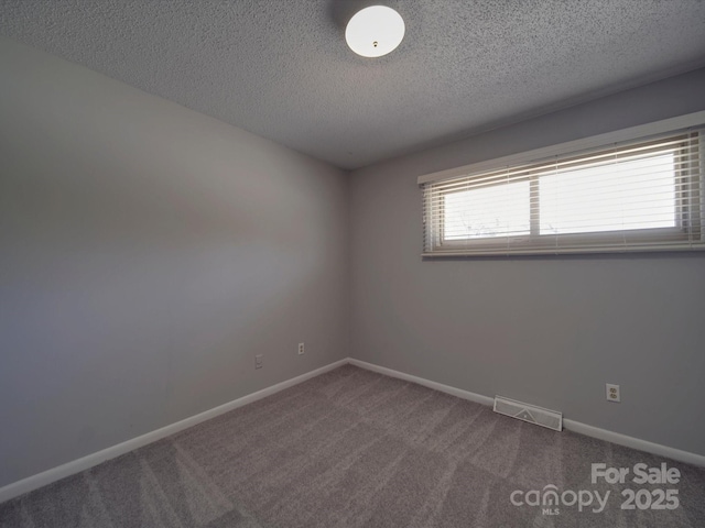 empty room featuring visible vents, carpet flooring, a textured ceiling, and baseboards