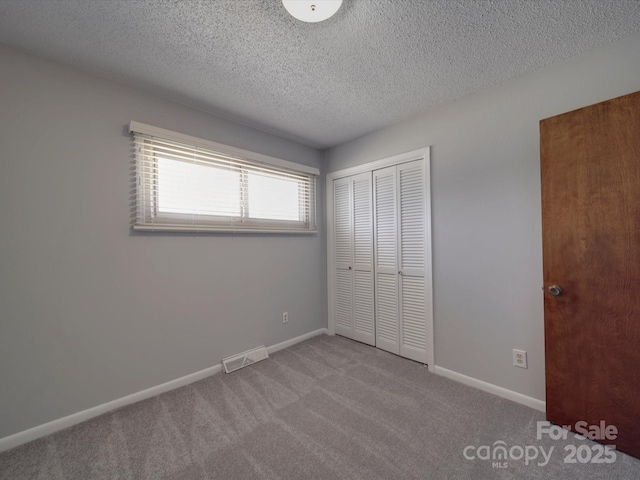 unfurnished bedroom with visible vents, a textured ceiling, a closet, carpet, and baseboards