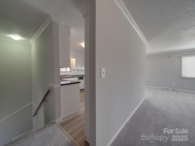 corridor with an upstairs landing, light carpet, a textured ceiling, and crown molding