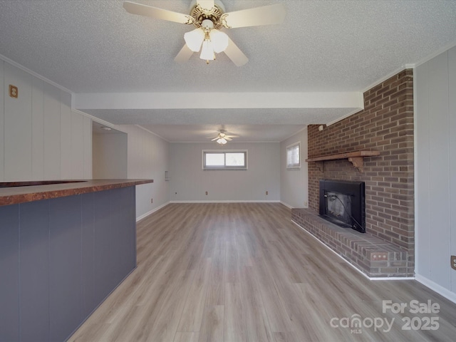 unfurnished living room with light wood-style flooring, ceiling fan, a textured ceiling, crown molding, and a brick fireplace