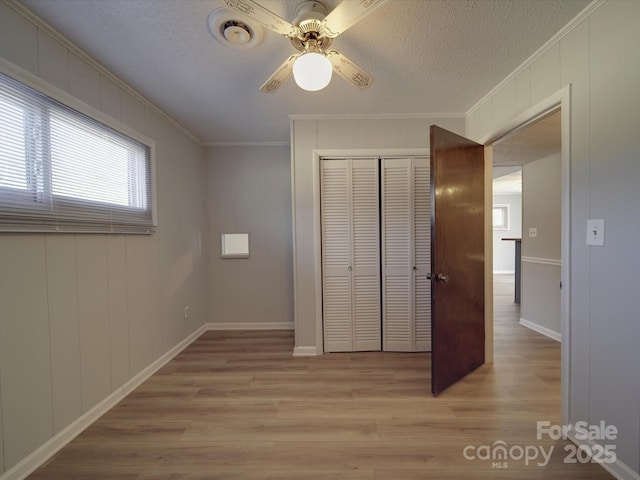 unfurnished bedroom featuring a textured ceiling, light wood-type flooring, a closet, and ornamental molding