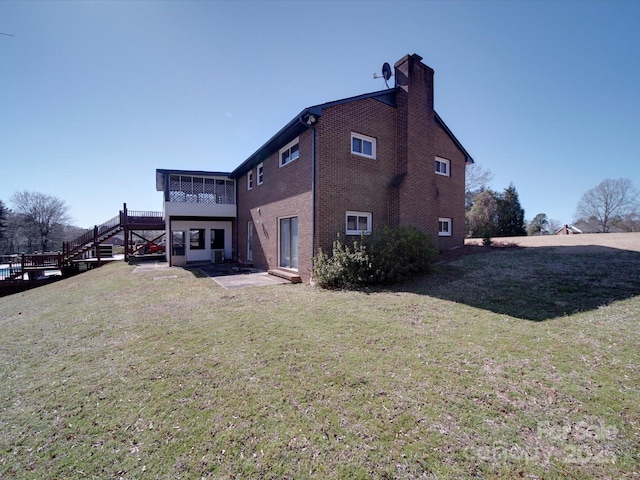 back of property with a patio, stairs, a yard, brick siding, and a chimney