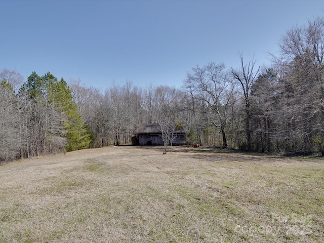 view of yard featuring an outdoor structure, a wooded view, and a barn