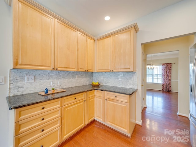 kitchen featuring backsplash, light brown cabinets, dark stone countertops, a chandelier, and light wood-type flooring