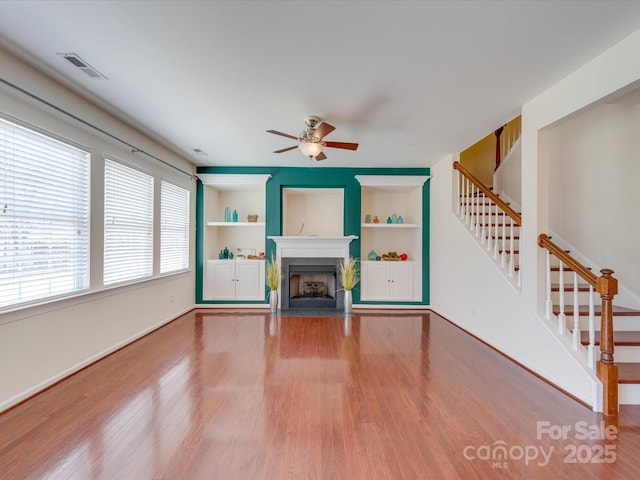 unfurnished living room with a fireplace with flush hearth, stairway, built in features, and wood finished floors