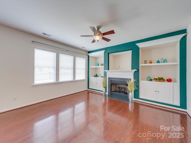 unfurnished living room featuring built in shelves, visible vents, a high end fireplace, wood finished floors, and baseboards