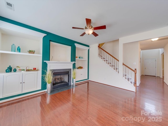 unfurnished living room featuring a fireplace with flush hearth, wood finished floors, visible vents, built in features, and stairway