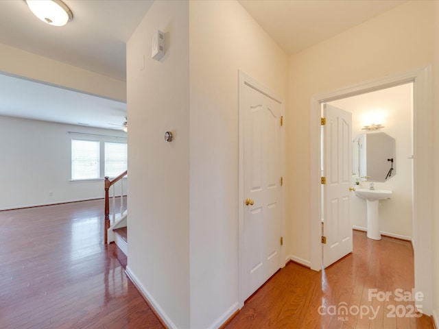 hallway featuring a sink, stairway, baseboards, and wood finished floors